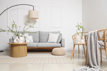 Interior of living room with grey sofa, table and blossoming branches in vases