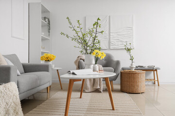 Interior of living room with grey sofa, daffodils and blossoming branches in vases
