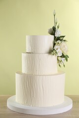 Delicious wedding cake decorated with flowers on wooden table against light green background, closeup