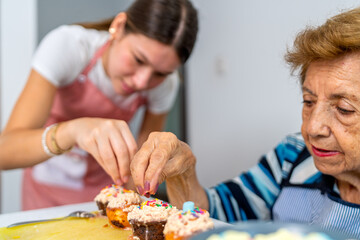 Grandmother and granddaughter decorating cupcakes together in the kitchen