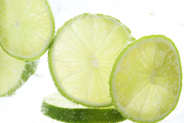 Refreshing soda water with slices of lime in glass on white background, closeup