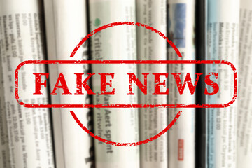 Red Fake News stamp and newspapers as background, closeup
