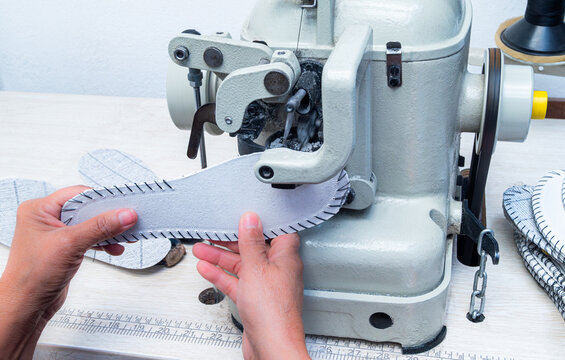 Woman's hands operating an industrial sewing machine to sew the leather sole for handmade shoes in the shoemaking workshop, close-up of the traditional shoemaking process. 