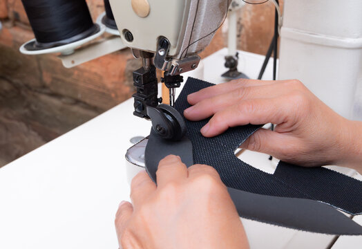A woman's hands sewing fabric with an industrial sewing machine in a shoemaking workshop. Close-up of the manual labor and textile manufacturing process.
