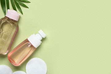 Bottles of micellar water, cotton pads and leaves on green background