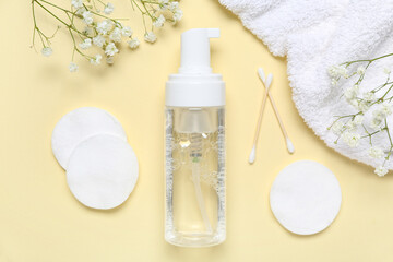 Bottle of micellar water, cotton pads, flowers and towel on beige background