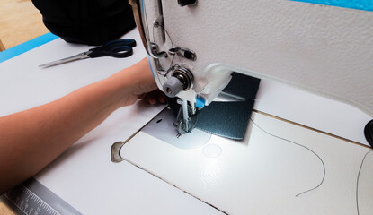 A woman's hands sewing fabric with an industrial sewing machine in a shoemaking workshop. Close-up of the manual labor and textile manufacturing process.
