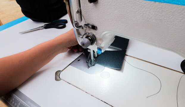 A woman's hands sewing fabric with an industrial sewing machine in a shoemaking workshop. Close-up of the manual labor and textile manufacturing process.