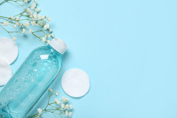 Bottle of micellar water, cotton pads and flowers on blue background