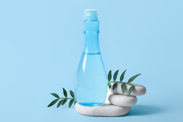 Bottle of micellar water, stones and leaves on blue background