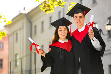 Couple of happy students with diplomas hugging on their graduation day