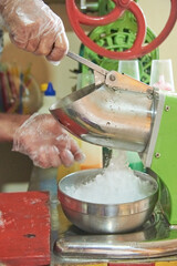 Unrecognizable person using an ice crusher machine to make a raspado, a sweet and refreshing Colombian snack composed of crushed ice with different sweet flavors and sauces or toppings.