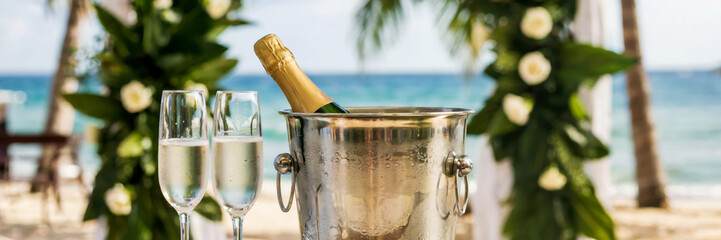 Champagne bucket with a chilled bottle of sparkling wine and two crystal champagne flutes, caribbean wedding celebration with floral tropical arch, long banner