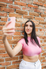 Young Hispanic woman taking a selfie against a brick wall