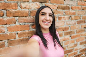 Latina LGBTQ young woman smiling in selfie pose near brick wall