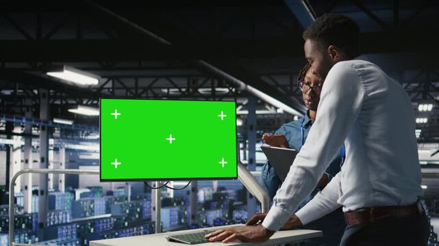 Server room coworkers doing brainstorming, using chroma key device to review diagnostics. Employees doing maintenance tasks in data center, looking at isolated screen monitor, camera A