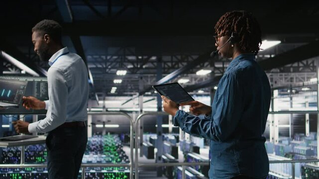 Server hub IT expert monitors systems, doing tech support, guiding users through troubleshooting steps. African american technician providing remote diagnostics using headset mic, camera A