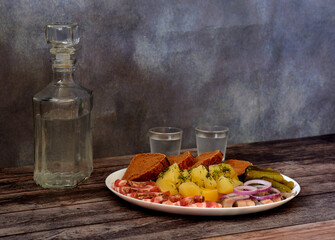 A glass decanter and two glasses of vodka on a dark wooden table and a plate with an assortment of...