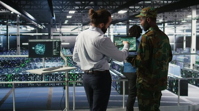 Military experts in data center reviewing drone surveillance feed on laptop screen. Army units in high tech server room doing battlefield reconnaissance operations using notebook, camera A