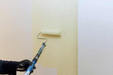 Person paints wall with light color using paint roller, showcasing home renovation effort in progress.