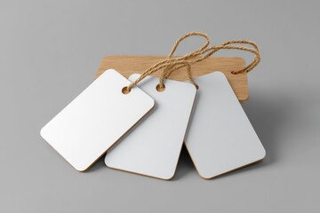 Three blank white rectangular tags with twine, attached to a small wooden backing, rest on a gray surface