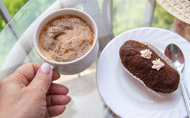 Female hand holding a cup of espresso coffee near a plate with chocolate brownie. Breakfast concept