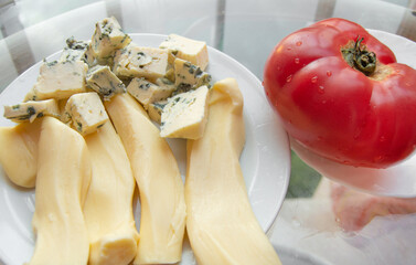 Different kinds of cheese on the plate and one red tomato, appetizers