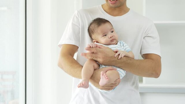 Asian devoted young father lovingly holds his three-month-old baby in a warm, inviting room. Their close bond radiates affection, peaceful atmosphere of comfort, safety, and unconditional love.