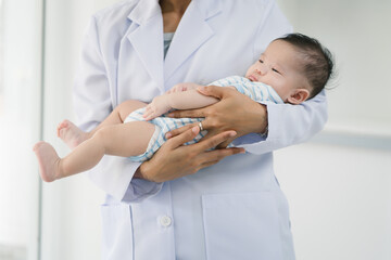 A young female doctor gently cradles a baby in her arms inside a bright room, exuding warmth,...