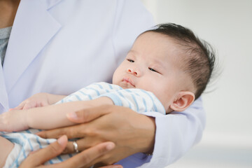 A young female doctor gently cradles a baby in her arms inside a bright room, exuding warmth,...