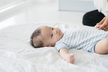 Asian loving young mother gently embraces her three-month-old baby in a cozy room, radiating warmth and affection. Their tender connection fills the space with a sense of comfort, security, and love.