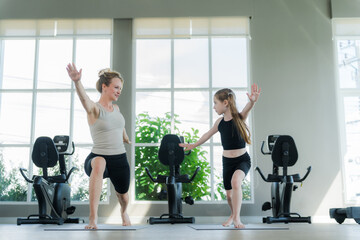 A girl stretches or exercises on a mat in a gym, with an instructor closely following her.