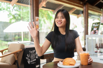 young woman having breakfast in cafe while waving hand
