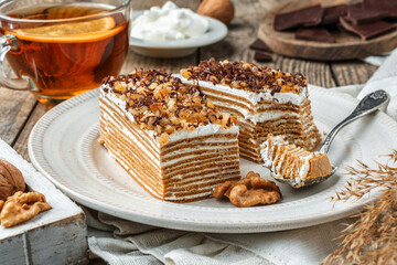 Homemade honey cake with sour cream and nuts on wooden background with cup of tea. Sweets, dessert...