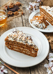 Delicious honey biscuit cake with cream, chocolate and nuts on wooden background with cup of tea and flowers. Sweets, dessert and pastry, homemade cakes, top view