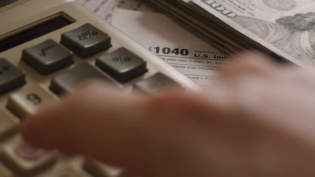 A close-up concept of tax accounting and income management, featuring a button calculator, U.S. tax Form 1040, and dollar bills on a desk