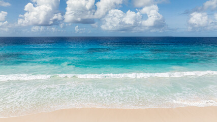 Turquoise waters and waves crashing onto a wide sandy beach. La Digue, Seychelles.