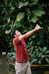 Young man makes hand gesture towards vibrant lush tropical plants