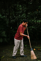 Dedicated man sweeping leaves in a lush green garden environment outdoors