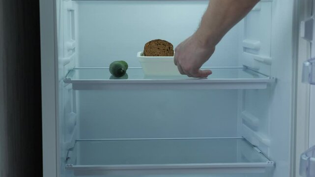 concept food shortage, empty container, piece of black bread and cucumber on the shelf of an empty refrigerator, crisis, hungry time