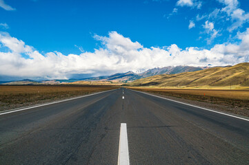 Breathtaking view of an open road leading to majestic mountains in Gorny Altay during a clear day with scattered clouds.