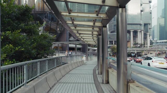 Hong Kong 20.02.2025 Scenic urban walkway in Hong Kong with contemporary architecture. Sidewalk features glass canopies, greenery, and nearby traffic. Captivating city view promotes exploration