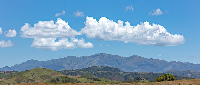 Panoramic view of rolling hills and mountains under a vast blue sky with fluffy clouds