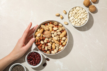 Beans, nuts and chia seeds in bowls and hand on light background, top view