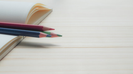A close-up side view of three colored pencils resting on the edge of an open notebook. Ideal for education, creativity, planning, or artistic inspiration themes.