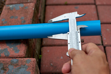 A close-up image of a person's hand using a vernier caliper to measure the diameter of a blue PVC...
