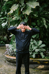 Playful man covering eyes in lush greenery garden setting