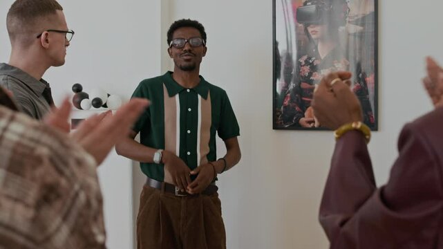 African American young artist talking about his paintings and bowing to adoring audience applauding in foreground