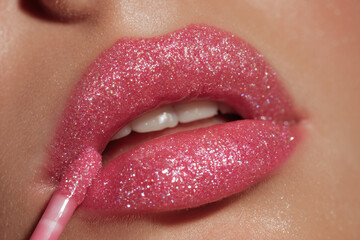 Naklejka premium Close up of lips with pink glitter lip gloss being applied with applicator for beauty and makeup concept