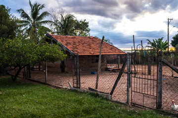 Rural scene in Brazil. Simple brick house with tile roof, surrounded by a wire fence. Evokes rural...